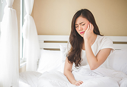 Woman sitting up in bed touching jaw in discomfort