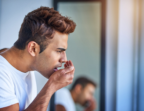 Man checking the smell of his breath using his hand.