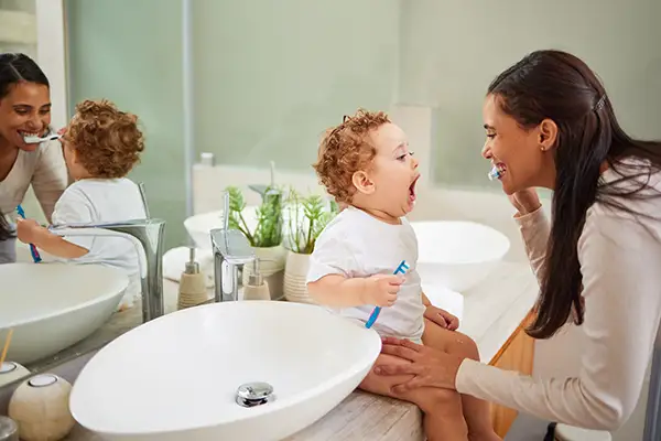 Mother and toddler brushing their teeth together in the bathroom, teaching early dental hygiene practices in a fun way.
